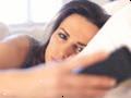 Olycklig kvinna i sängen ser på sin mobiltelefon