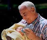 Bild av en farfar håller sin nyfödda barnbarn, mata honom en flaska